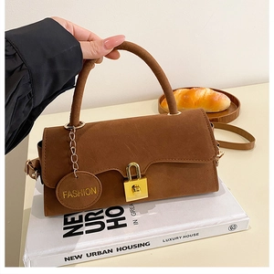 Détail d'un sac à main en daim marron avec serrure dorée et étiquette de mode sur livres