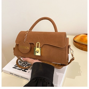 Détail de la texture en daim marron avec boucle dorée et pendentif mode sur le sac
