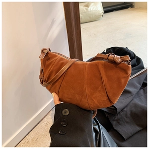 Detail of a brown suede crescent bag featuring chic vertical pleats and knot strap detail