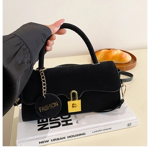 Détail du sac bandoulière en daim noir avec serrure dorée et pendentif sur un livre