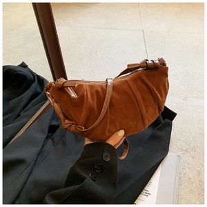 Detailed close-up of brown suede dumpling bag with knotted shoulder strap and pleats