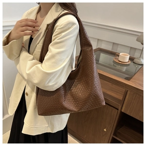 Detailed view of dark brown woven leather tote bag shown on a shoulder over corduroy jacket