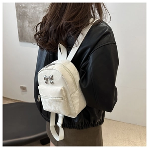 Détail du mini sac à dos blanc texturé avec un nœud décoratif en métal argenté