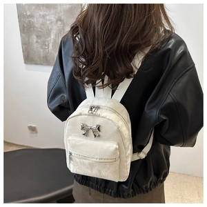 Gros plan d'un mini sac à dos blanc avec nœud argenté et texture plissée sur le mannequin