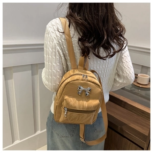 Mini sac à dos kaki avec charm nœud argenté porté par un mannequin dans un décor intérieur