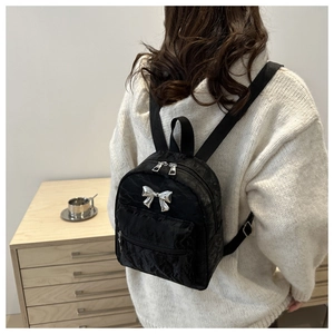 Détail d'un mini sac à dos noir avec nœud métallique et texture plissée porté par un modèle