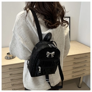 Mini sac à dos noir avec texture plissée et nœud métallique argenté porté par le modèle