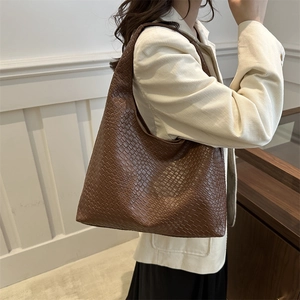 Minimalist large brown woven leather tote bag with wide strap on a model's shoulder