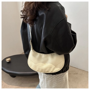 Close-up of beige crescent shoulder bag in lychee pattern leather worn by a model