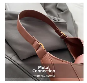 Detail of gold metal ring connecting the leather strap and body of a brown baguette bag