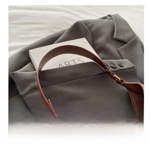 Detail of the brown leather curved handle on a minimalist shoulder bag with smooth texture