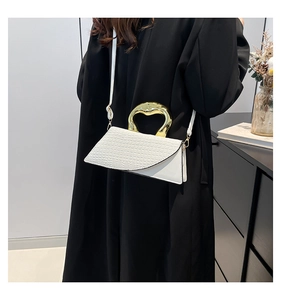 White crocodile embossed crossbody bag with a sculptural gold metal handle on a black coat