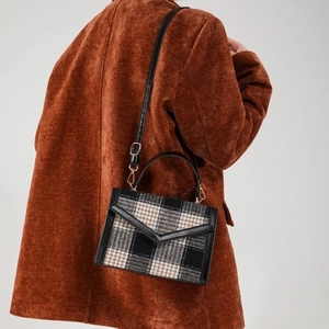 Sac bandoulière rétro à carreaux avec détails en cuir porté sur un manteau marron