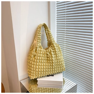 Detailed close-up of yellow popcorn textured pleated shoulder bag on white display