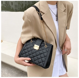 Detail of black quilted shoulder bag with gold metal buckle and elegant chain strap