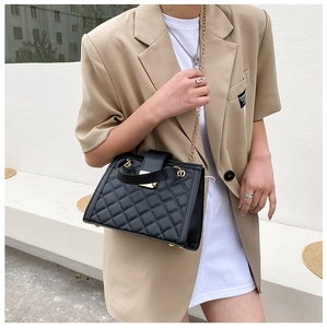 Detail of black quilted leather shoulder bag with gold chain strap on a model