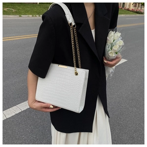 Detail of white crocodile pattern tote bag featuring gold chain and metallic frame decor