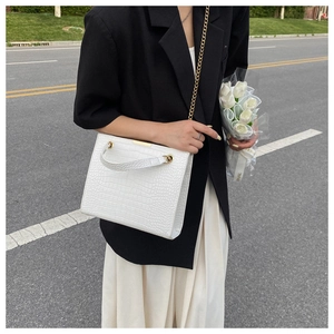 White crocodile pattern tote bag with gold chain and handle held by model in black blazer