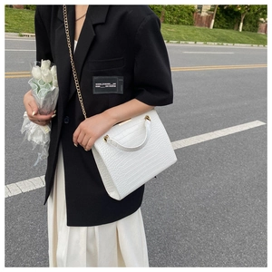Outdoor shot of a white crocodile embossed tote bag with gold chain strap detail