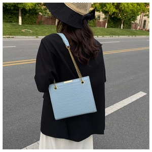 Detail of light blue croc-embossed leather tote with gold chain strap for women