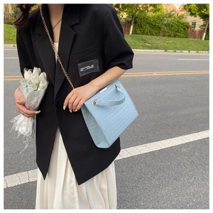 Detail of light blue crocodile-textured shoulder bag with gold chain and metal handle