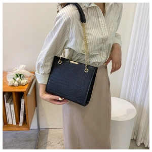 Detail of black crocodile texture tote bag with elegant golden chain shoulder strap