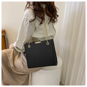 Detail of black crocodile texture tote bag with gold chain strap on model