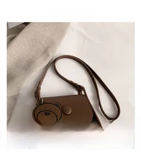 Detailed close-up of brown crossbody bag with flap cover and cute bear keychain