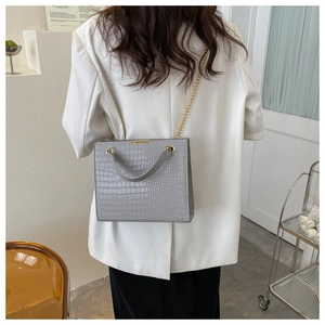 Detail of grey crocodile embossed tote bag with gold chain strap on a model