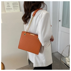 Detail showing bright orange crocodile pattern bag with gold chain and metal bar accents