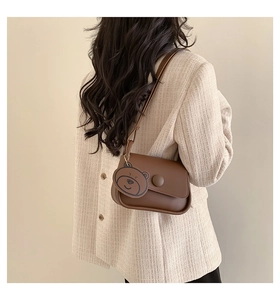 Detail of brown vintage crossbody bag with flap closure and cute bear charm accent