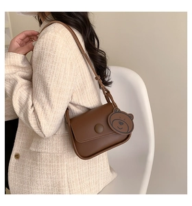 Detail of a brown leather shoulder bag with flap closure and cute bear charm accessory