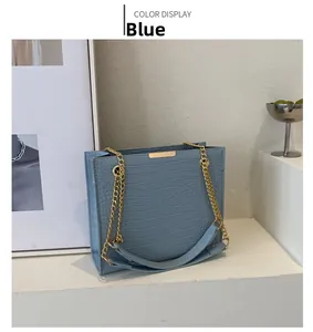 Detail of blue crocodile pattern handbag featuring gold chain strap and square structure
