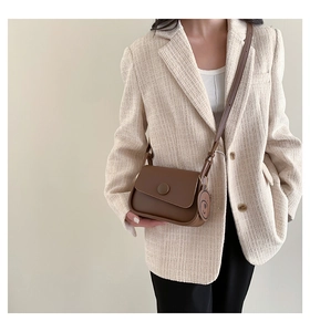 Detailed view of a brown leather crossbody bag with a round buckle and cute bear charm