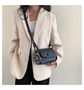 Detail of a black leather crossbody bag featuring a matte finish and a cute bear charm