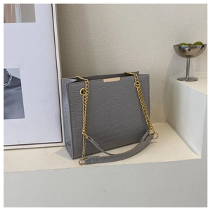 Detail of grey crocodile pattern texture and golden chain strap on square tote bag