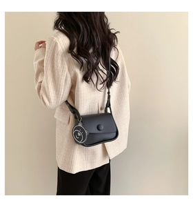 Detail of a black leather crossbody bag with a matte finish and a cute bear charm pendant