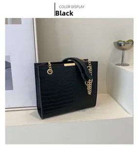Detail of black crocodile texture tote bag with gold chain strap and metal trim