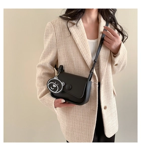 Detail of a vintage black leather crossbody bag with a cute bear charm on a female model