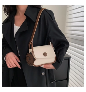 Minimalist cream shoulder bag with brown bear charm worn over a classic black coat