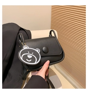Detail of black textured crossbody bag with round buckle and cartoon bear charm