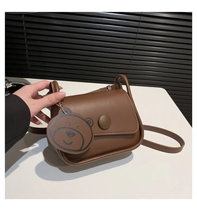 Detail of dark brown leather crossbody bag featuring a round button and bear charm