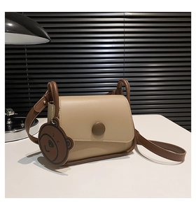 Macro shot of a vintage leather crossbody bag with brown bear charm and metal buckle detail