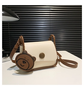 Detail of a minimalist cream shoulder bag with brown straps and cute bear charm