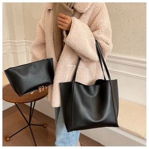 Détail d'un grand sac cabas en cuir noir et pochette porté avec un manteau beige