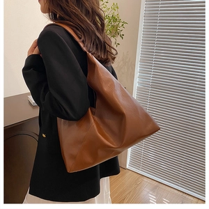 Brown soft leather tote bag worn by a model in a warm indoor natural light setting