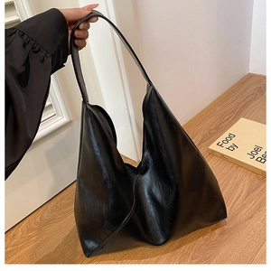 Detail of minimalist black tote bag featuring glossy leather texture and stylish pleats