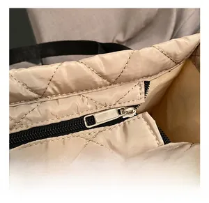 Detail showing smooth black metal zipper and quilted nylon texture of the beige tote bag