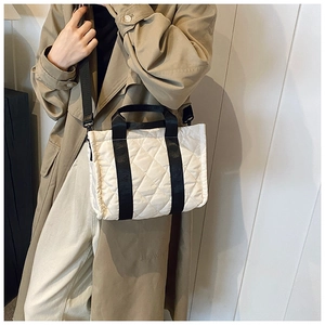 Dettaglio borsa tote trapuntata bianca con manici neri indossata su un trench kaki