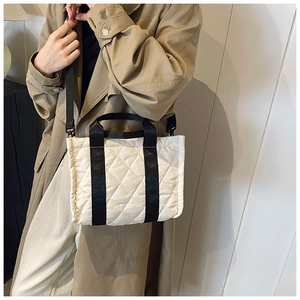 Detail of cream quilted tote bag featuring black woven handles and diamond stitching